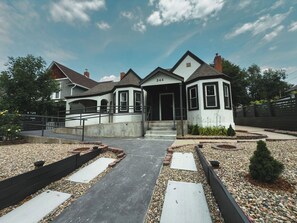 A two-story building with a white facade, a black roof, and a number '544' on the front. There is a paved entrance with steps leading up to the door. - Traveler’s Dream Home! Hot tub, Firepit, & BBQ (Colorado Springs)