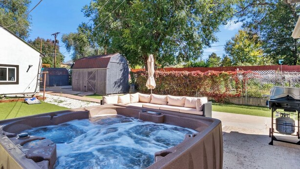 A hot tub in a backyard with a lawn, a covered outdoor seating area, and a fence.