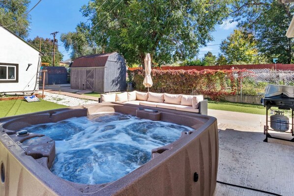 A hot tub in a backyard with a lawn, a covered outdoor seating area, and a fence.
