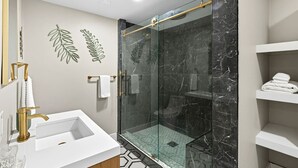 A modern bathroom with a glass-enclosed shower, a white sink, and marble walls.