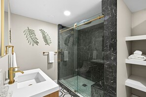 A modern bathroom with a glass-enclosed shower, a white sink, and marble walls.