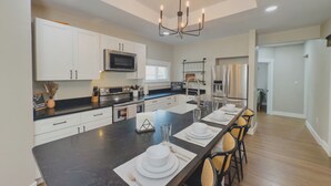 Una cocina moderna con armarios blancos, una isla central y un comedor dispuesto para seis personas.