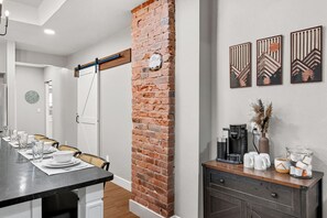 Een zithoek met een wand van baksteen, een koffiehoek en uitzicht op de aangrenzende ruimte.