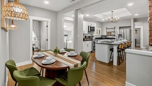 A modern kitchen with white cabinets, a central island, and a dining area with green chairs.