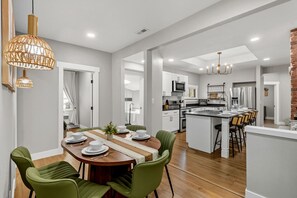 A modern kitchen with white cabinets, a central island, and a dining area with green chairs.