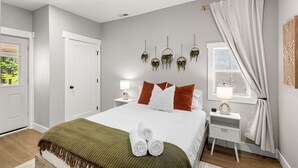 A modern bedroom with a bed, bedside tables, a window with curtains, and wall-mounted planters.