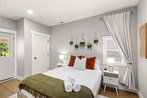 A modern bedroom with a bed, bedside tables, a window with curtains, and wall-mounted planters.