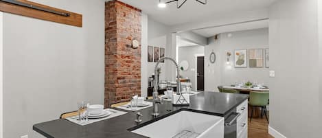 A modern kitchen with a central island, a brick accent wall, and a dining area in the background.