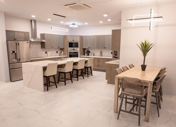 A modern kitchen with a central island, stainless steel appliances, and a dining area with wooden chairs.
