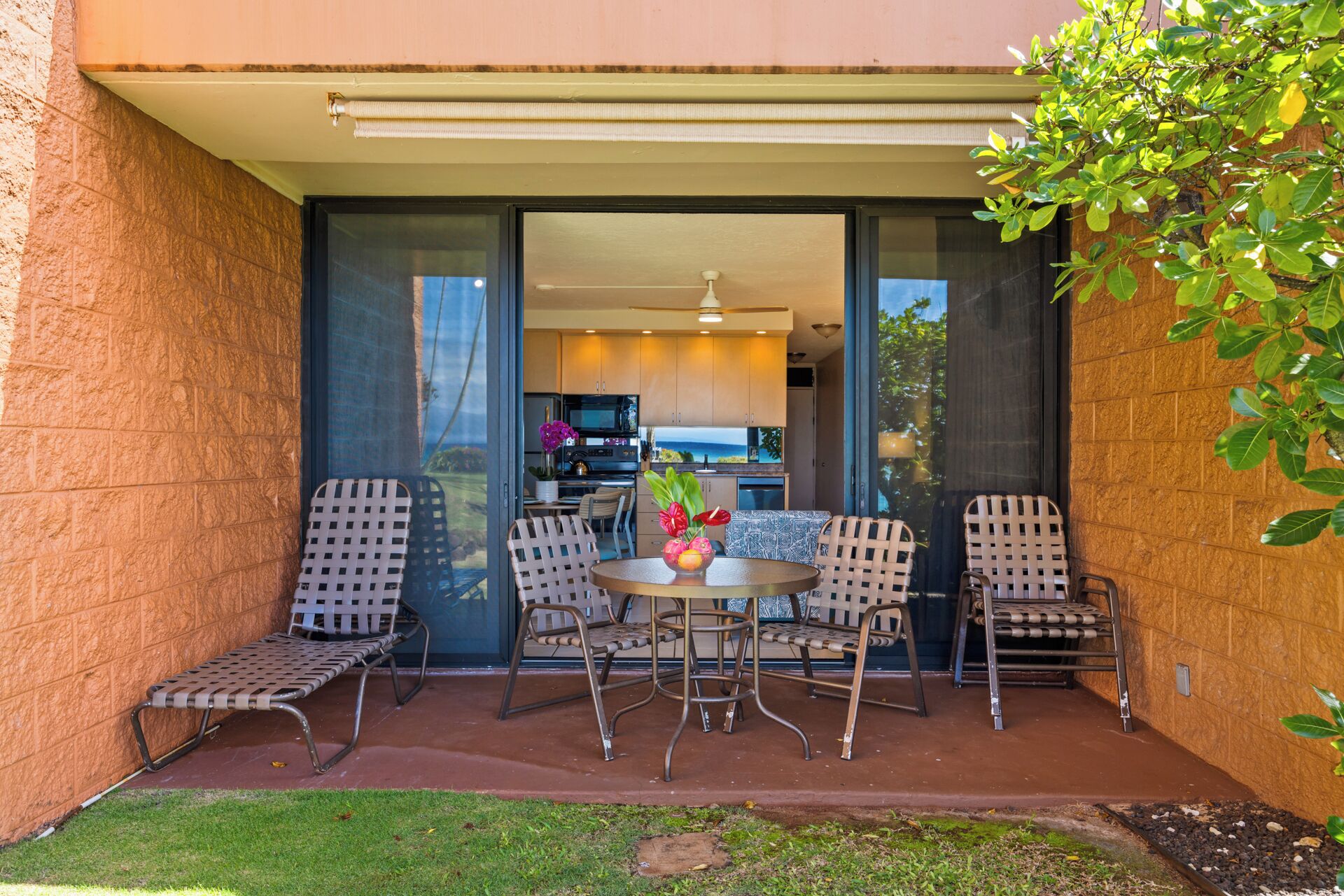 A patio with a table and chairs, a view of the kitchen, and a small garden area.