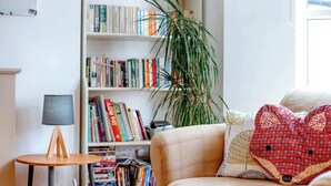 Una sala de estar acogedora con una estantería, una mesa redonda de madera y una planta grande.