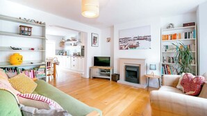 Una sala de estar moderna con chimenea, televisión y cocina al fondo.
