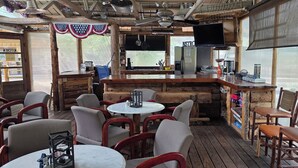 A rustic wooden interior with round tables and chairs, a bar area with a television, and a kitchen visible through a window. - Modern Suite with Rustic Charm Dog Friendly Suite with King Bed and Full Kitchen (Cedaredge)