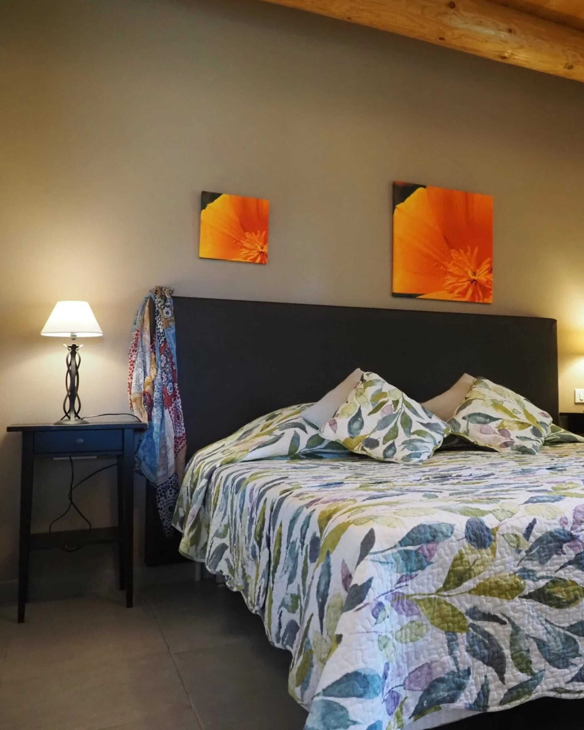 A bedroom with a bed, a nightstand, a lamp, and two wall art pieces.