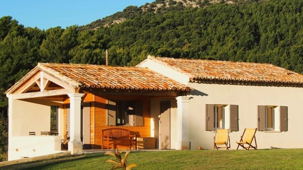 A two-story house with a tiled roof, a porch with a wooden bench, and a grassy lawn. - Villa Garance with air conditioning (bedroom, living room, and kitchen) (LE BARROUX)