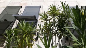 A rectangular swimming pool with clear blue water, surrounded by a tiled deck. There are several lounge chairs aligned along the pool's edge, and a row of potted plants in the foreground. - Villa Garance with air conditioning (bedroom, living room, and kitchen) (LE BARROUX)