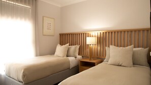 Habitació d'hotel amb dos llits, un panell de fusta al capçal, una taula de nit amb una làmpada i un quadre al mur.