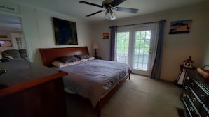 Ein Schlafzimmer mit einem Bett, einem Deckenventilator, einem Schreibtisch, einer Lampe und einem Fenster mit Vorhängen.