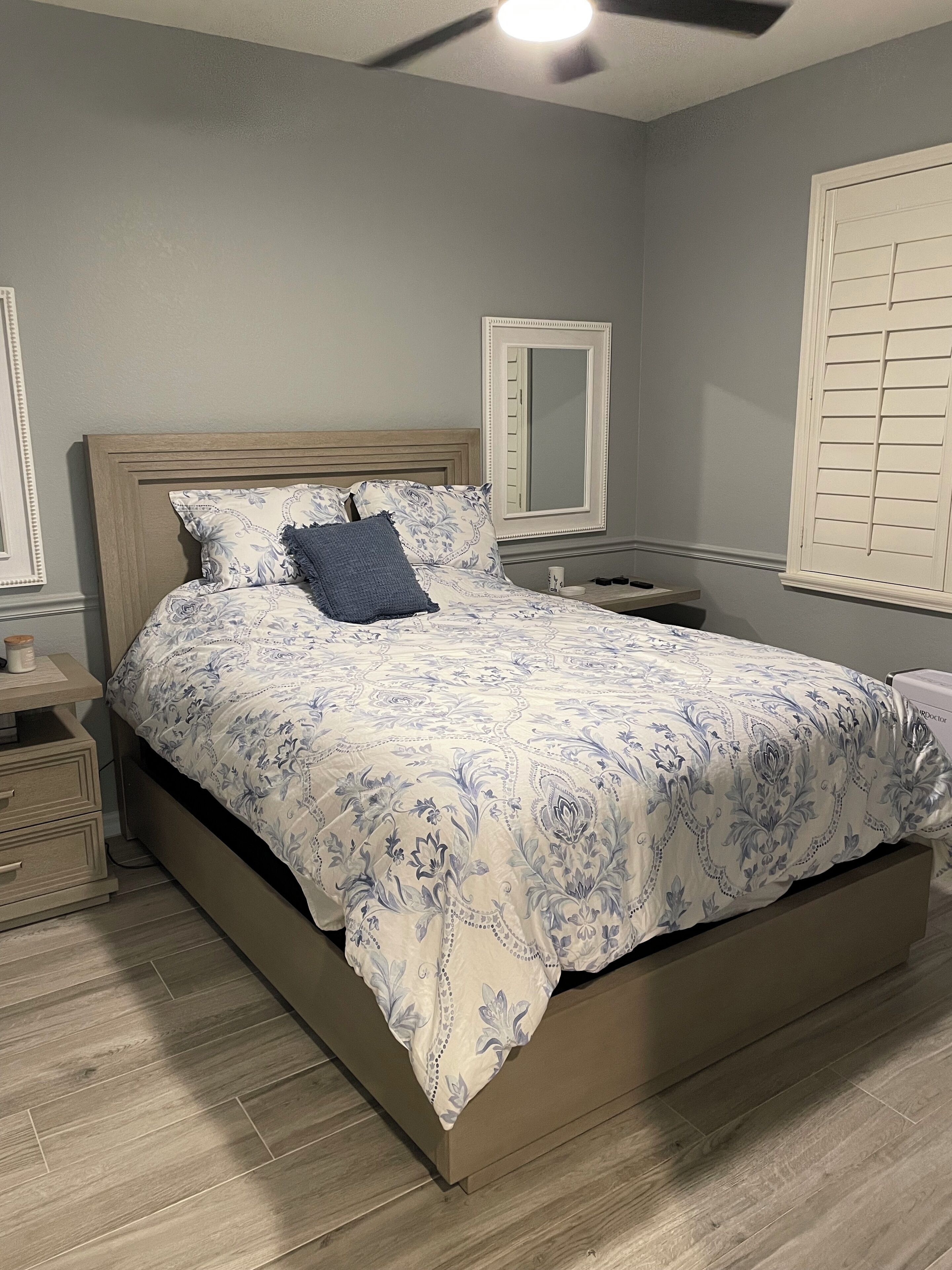 Une chambre à coucher comprenant un lit, des tables de chevet, une commode, un miroir et une fenêtre avec des volets.