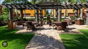 An outdoor patio area with tables and chairs, surrounded by palm trees and a pergola structure. - Charming 3-bedroom townhome on a quad in amazing Paseo in Fort Myers (Fort Myers)