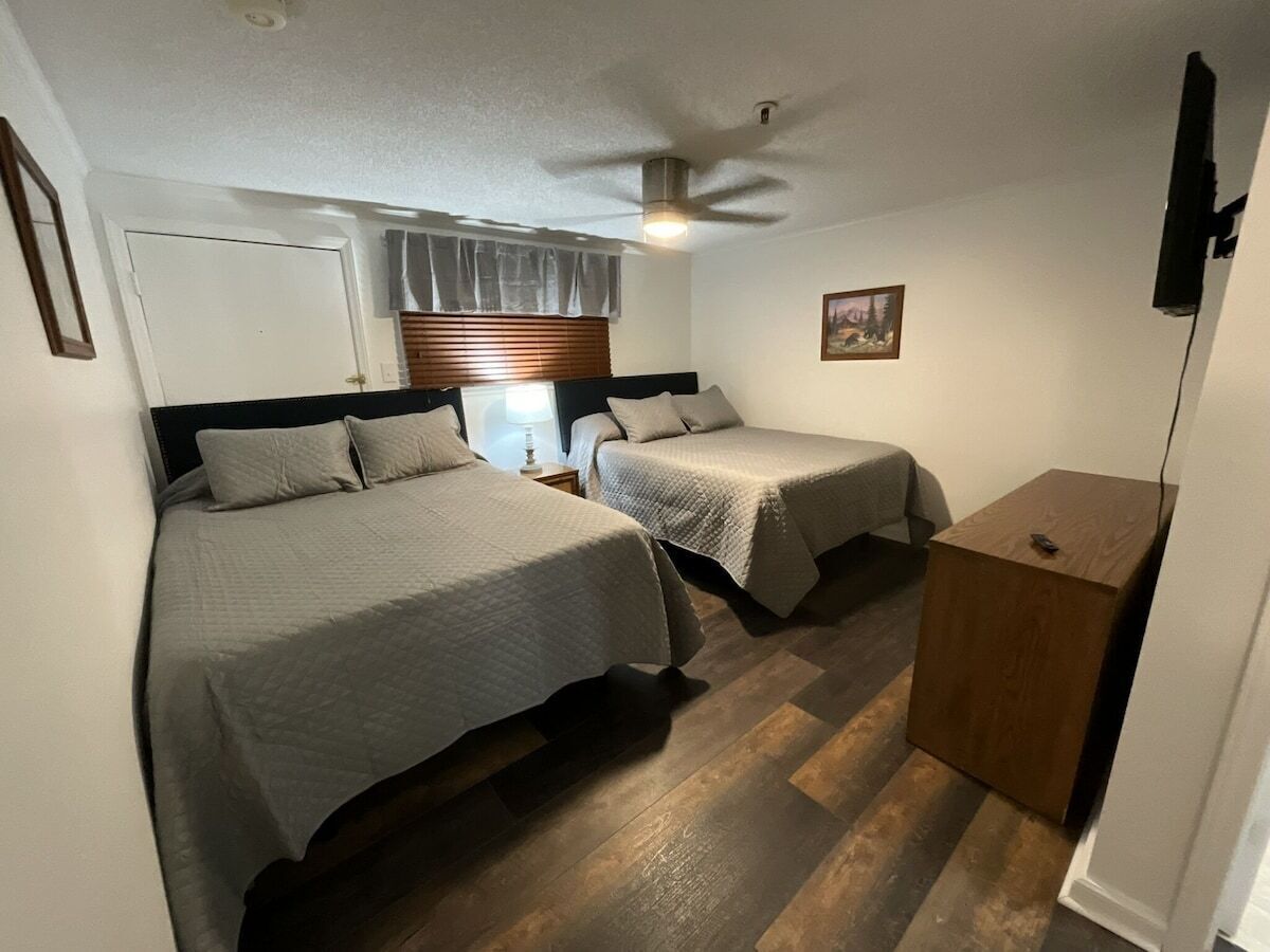 Ein Zimmer mit zwei Betten, einem Deckenventilator, einem Holzschrank und einem gerahmten Bild an der Wand.