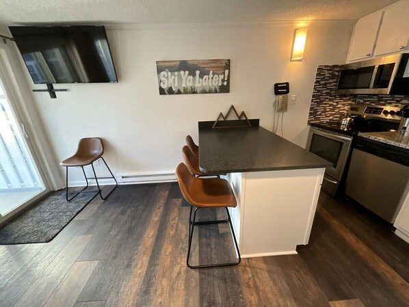 Eine moderne Küche mit Kochinsel, einem Flachbildfernseher an der Wand und Barhocker an der Kücheninsel.