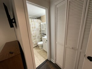 A narrow hallway leading to a bathroom with a toilet, shower curtain, and a white cabinet.