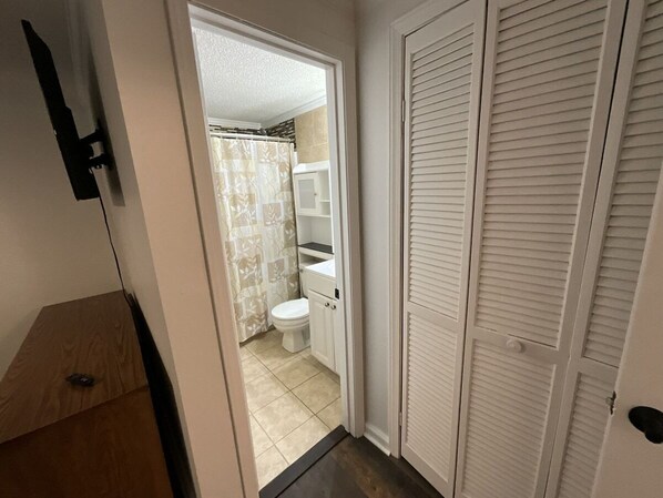 A narrow hallway leading to a bathroom with a toilet, shower curtain, and a white cabinet.