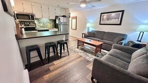 Et moderne køkken med en bar, en grå sofa og et tæppe med et mønster.