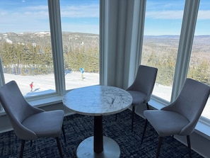 Una habitación con una mesa redonda y dos sillas, ventanas grandes con cortinas, y vistas a un paisaje nevado.