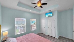 Un dormitorio con cama, ventilador de techo, televisor y ventana con persianas.