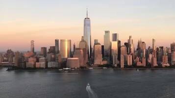 Stadszicht met een opvallend wolkenkrabber, vermoedelijk One World Trade Center, en een wateroppervlak op de voorgrond.
