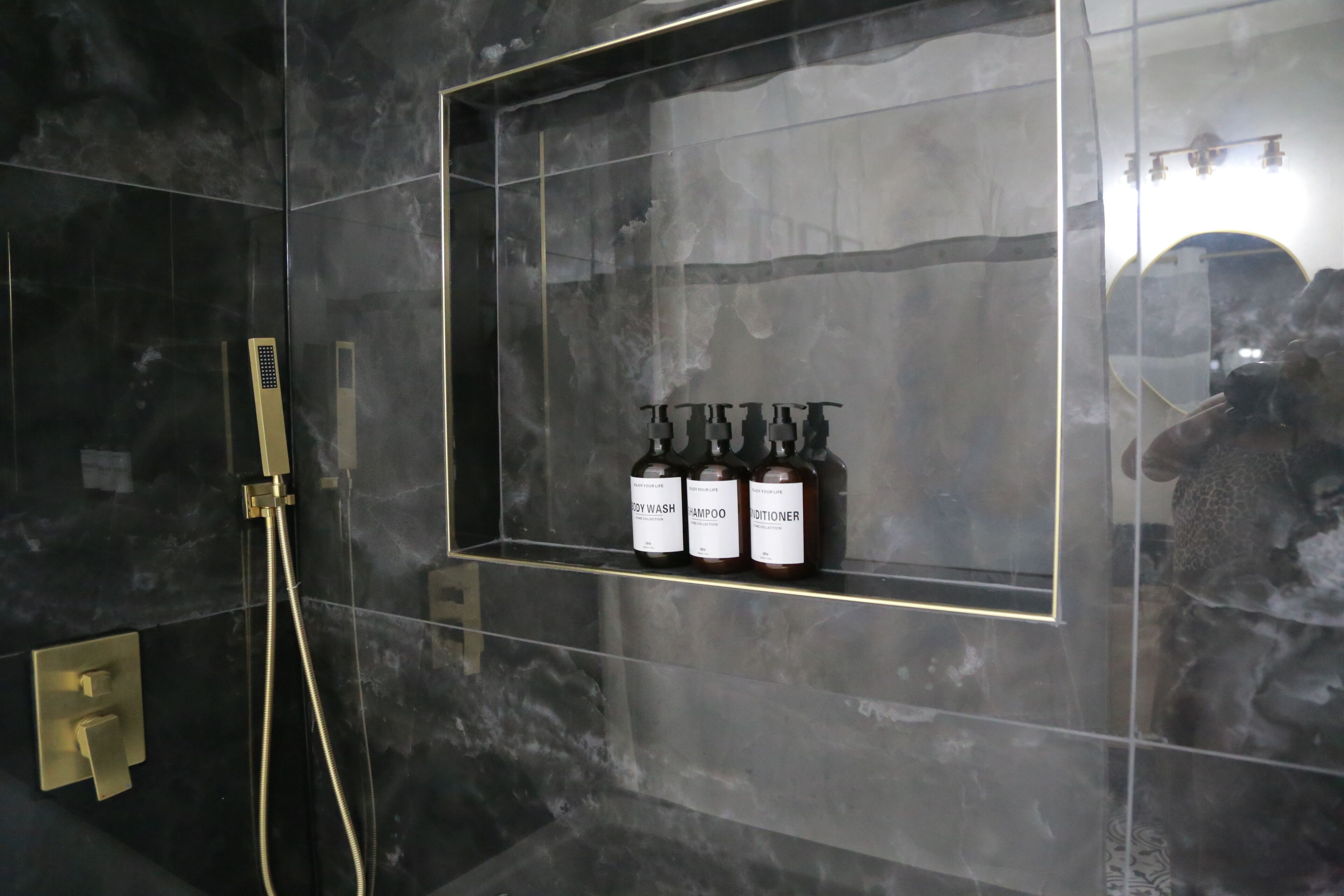 A bathroom with a glass-enclosed shelf holding three bottles labeled "SHAMPOO," "SHAMPOO," and "SHAMPOO."