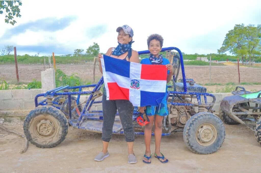 Dos personas sostienen una bandera frente a un vehículo azul.