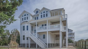 A multi-story building with a balcony on the second floor, a covered porch, and a staircase leading to the entrance. - 7138- Legasea, - Coastal Escape w/ Ocean Views & Private Pool (Waves)