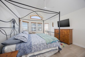 Un dormitorio con cama con dosel, cómoda de madera, televisor en la pared y ventana con persianas.