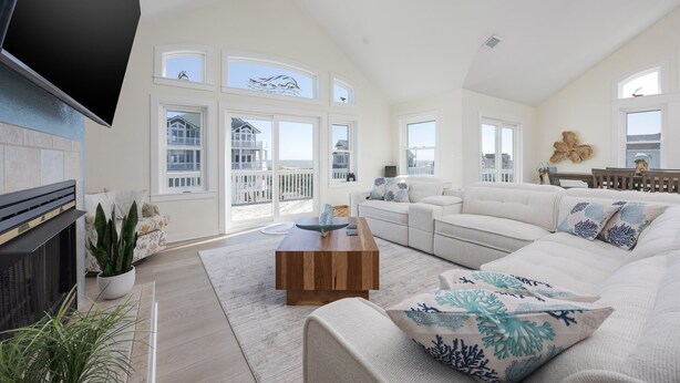 A spacious living room with a large flat-screen TV, a fireplace, and a view of the balcony. - 7138- Legasea, - Coastal Escape w/ Ocean Views & Private Pool (Waves)