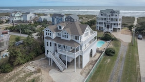 A large, multi-story house with a balcony and a swimming pool, located near a beach. - 7138- Legasea, - Coastal Escape w/ Ocean Views & Private Pool (Waves)