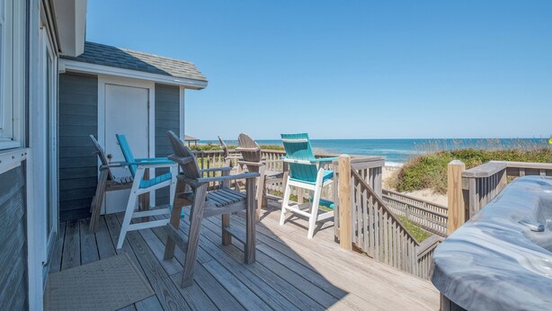 Eine Holzterrasse mit Stühlen mit Blick auf einen Strand.