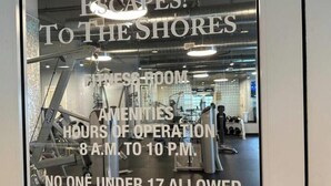 Une salle de remise en forme équipée, une pancarte indiquant « ÉVADEZ-VOUS ! VERS LES PLAGES », et un avis précisant que la salle est ouverte de 8 h à 22 h, et que l’accès est interdit aux personnes de moins de 17 ans.