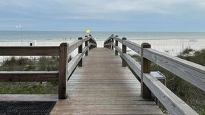 Une promenade en bois menant à une plage, avec un drapeau visible au loin.