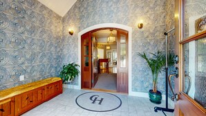A hotel lobby with patterned wallpaper, a wooden bench, potted plants, and a circular emblem on the floor. - The Crocker House Country Inn (Rm 3) (Hancock)