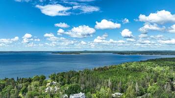 A coastal property with a large house surrounded by dense forest, overlooking a vast body of water and distant land.