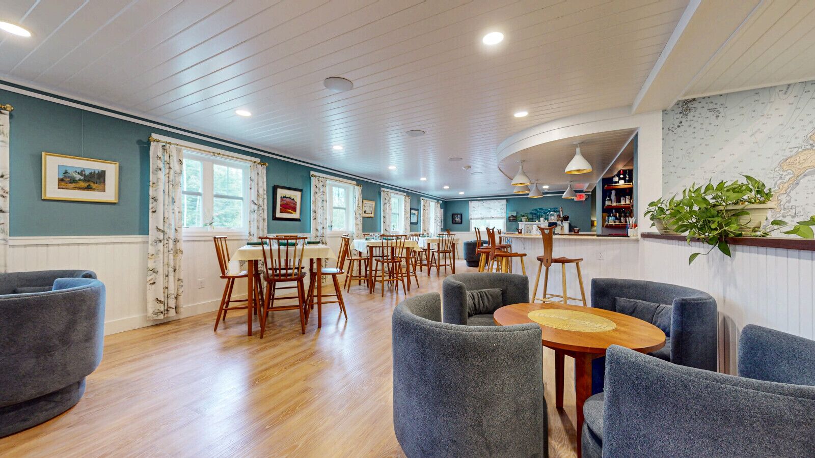 A spacious dining area with wooden tables and chairs, a bar area with a counter and stools, and a large window with curtains.