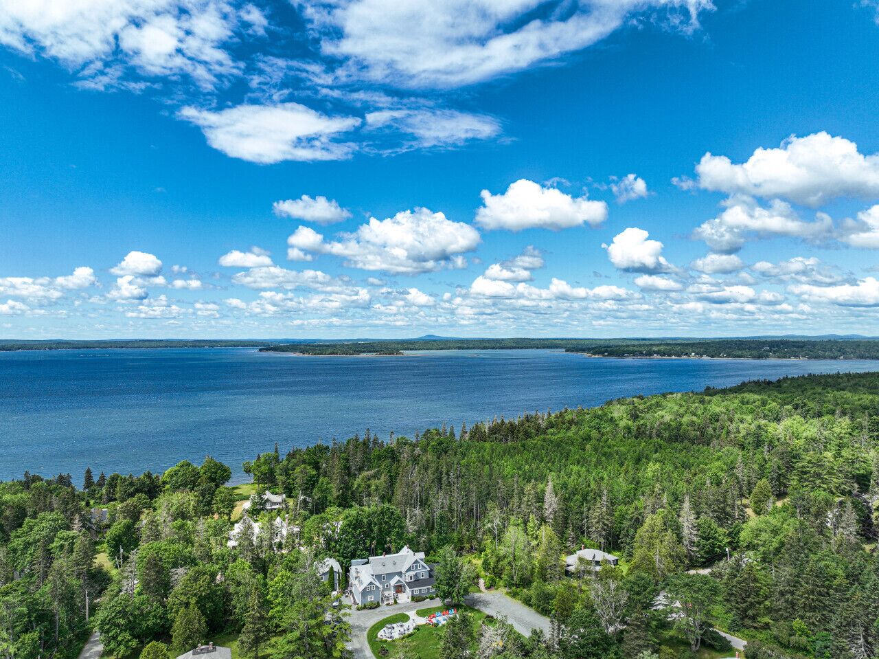 Une propriété située sur la côte, avec une grande maison entourée d’une forêt dense, offrant une vue imprenable sur une vaste étendue d’eau et sur la terre ferme au loin.