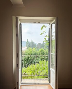 Puerta abierta que da a un balcón con vistas a zonas verdes y edificios.