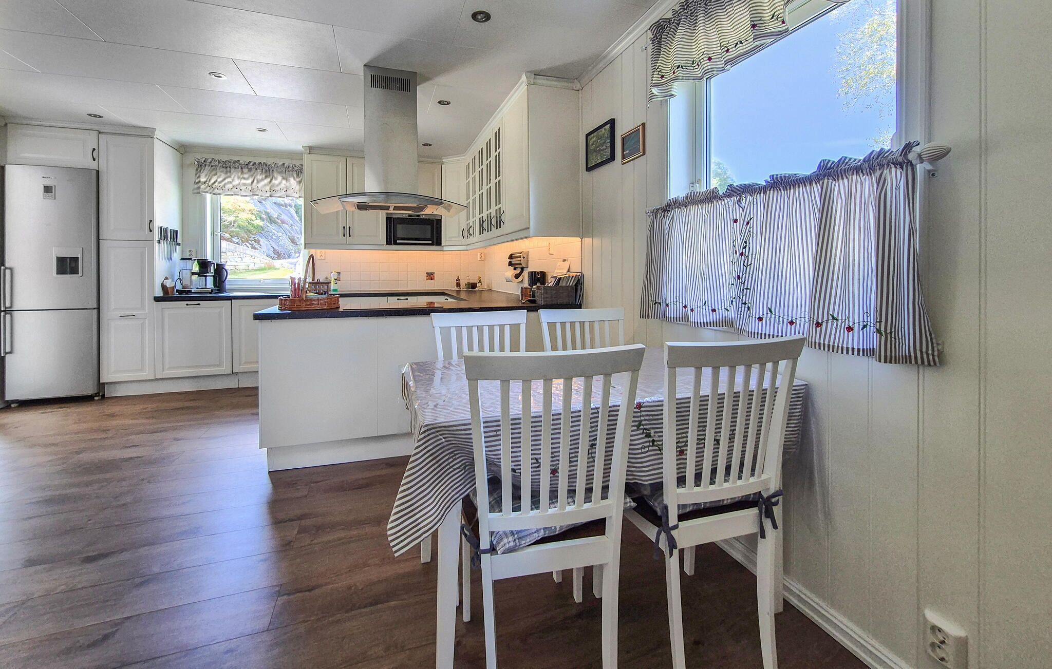 A kitchen with white cabinetry, a central island, and a dining area with white chairs.