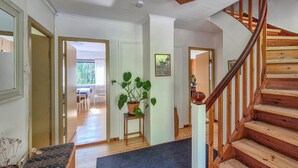 A staircase leading to an upper floor, wooden flooring, a potted plant, and a dining area with natural light.