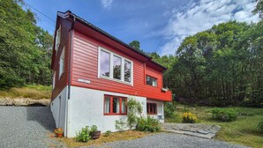 A two-story house with a red exterior and white trim, surrounded by a forested area.