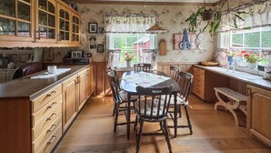 Una cocina tradicional con armarios de madera, una mesa de comedor con sillas y un ventanal con cortinas.